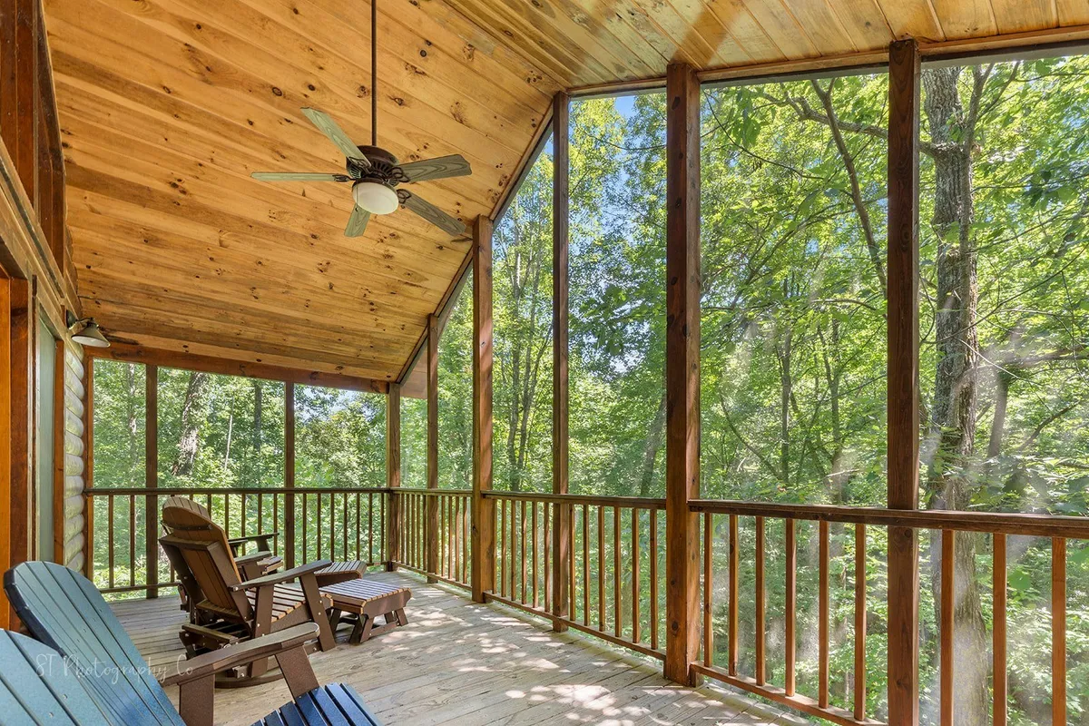 This image features a serene corner with outdoor chairs positioned by expansive windows, emphasizing the seamless connection between interior comfort and the wooded views outside. Soft morning or evening light filters through the trees, hinting at the tranquil setting.