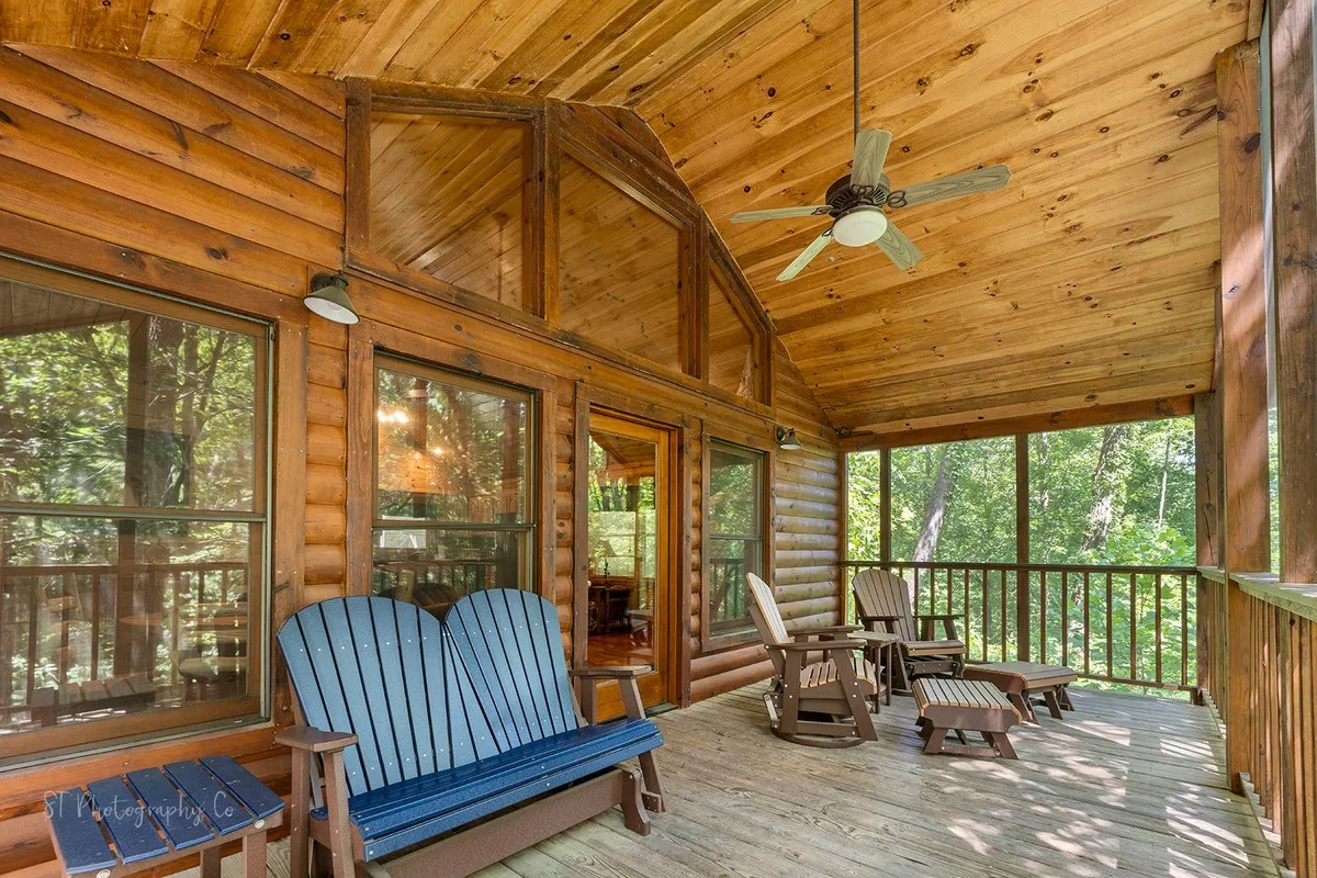 An exterior porch scene with classic wooden rocking chairs, a wooden ceiling, and large windows overlooking the natural surroundings. The setup encourages relaxation and immersion in the mountain setting, symbolizing the connection between cabin privacy and the outdoors.