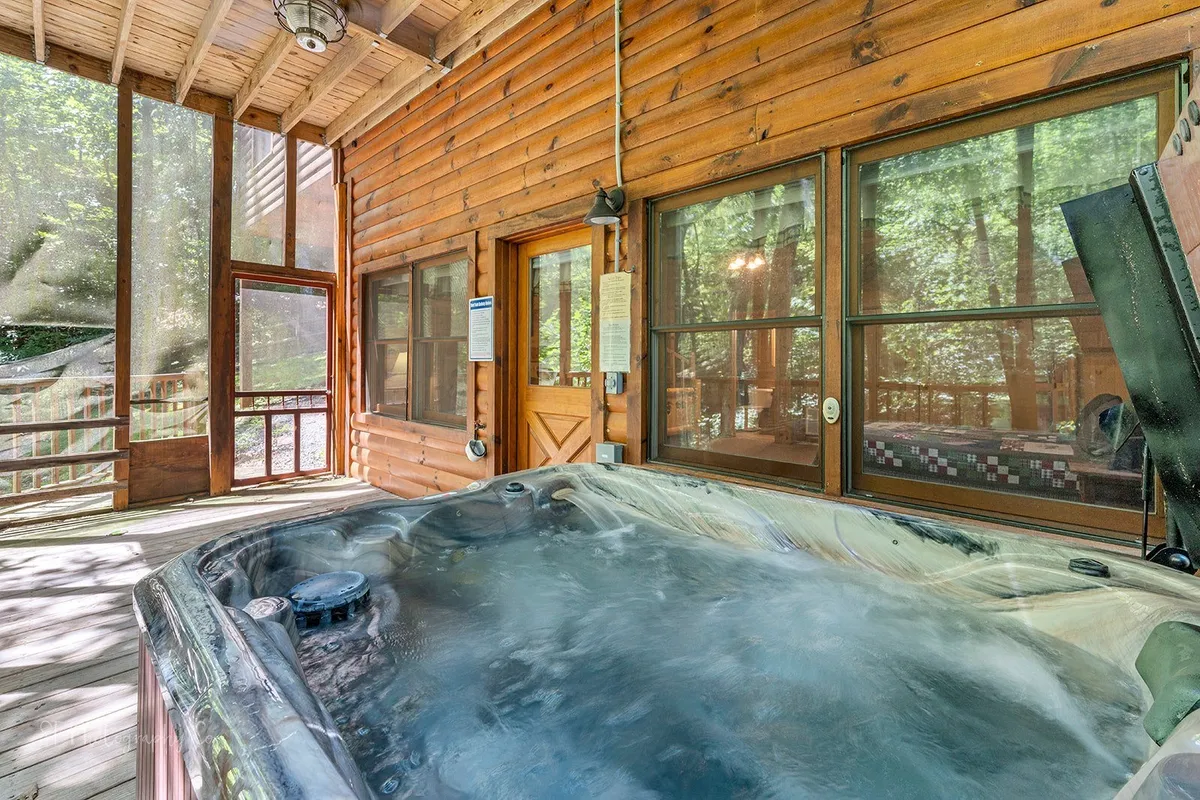 This image showcases a bubbling indoor hot tub set against wooden walls and large windows, allowing natural light to pour in and offering views of the surrounding nature. The peaceful setting invites guests to relax in privacy while enjoying the outdoors from the comfort of the cabin.