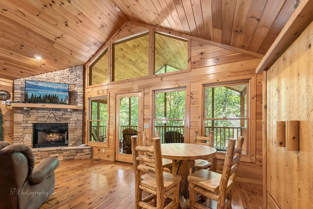 A spacious living area featuring a cozy fireplace, expansive wooden dining table, and large windows that invite natural light and reveal glimpses of the outdoors. The setting is arranged for gatherings, with comfortable seating perfect for group activities or relaxing after a day of adventure.