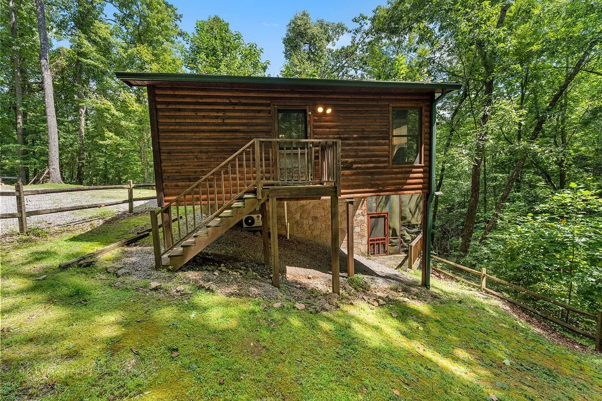 This image features a log cabin structure with a stairway entrance surrounded by vibrant greenery. The outdoor deck and natural surroundings create an inviting space to drink morning coffee or prepare for a day of hiking with pets. The view from the deck offers a sense of immersion in nature.